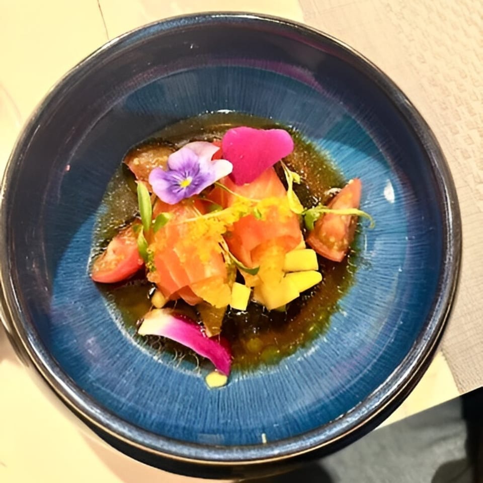 Japon's salmon sashimi with mango, cherry tomatoes, and edible flowers in a blue bowl.