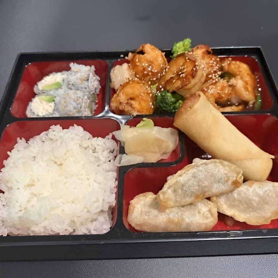 Japon bento box with shrimp, sushi, rice, spring roll, dumplings, and pickled ginger.