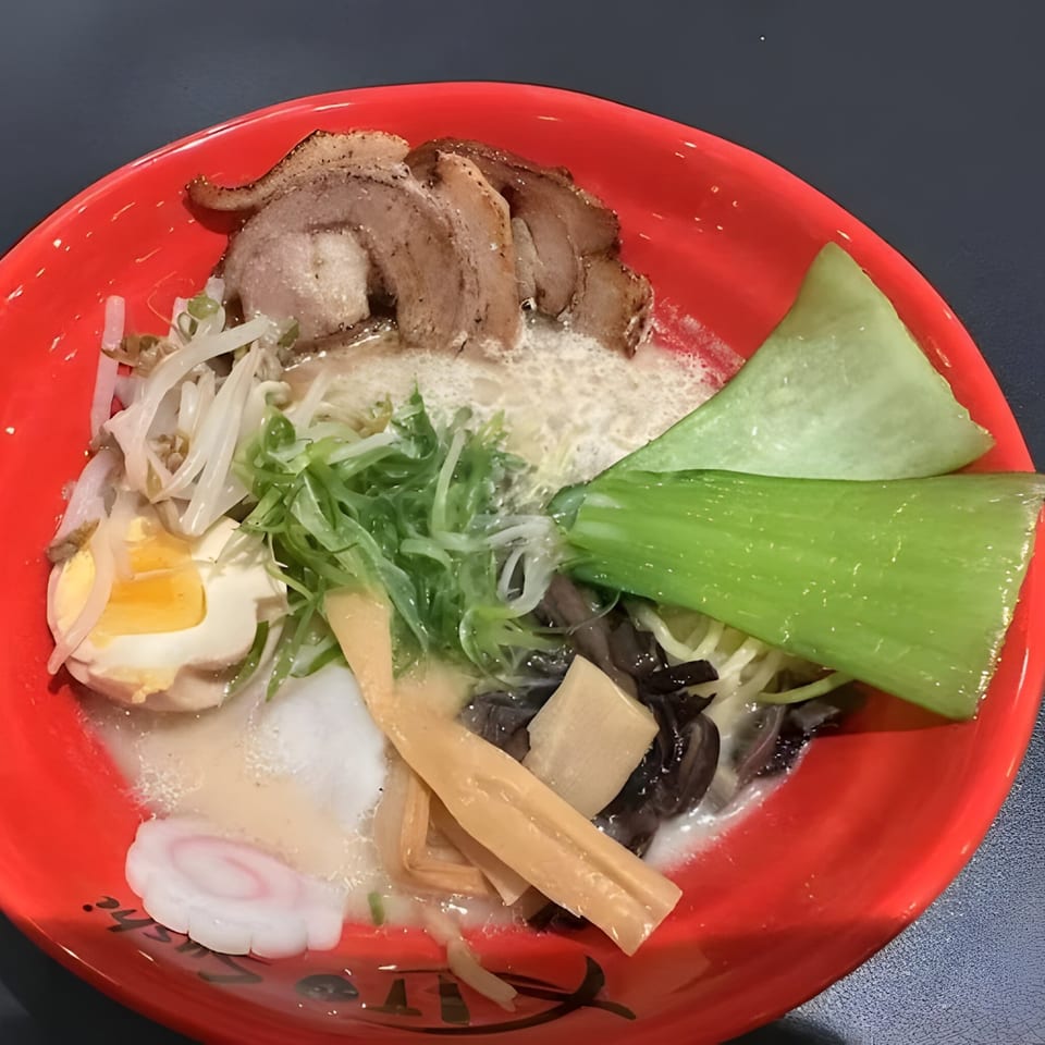 A vibrant red bowl of Japanese ramen with pork, egg, bok choy, and other toppings.
