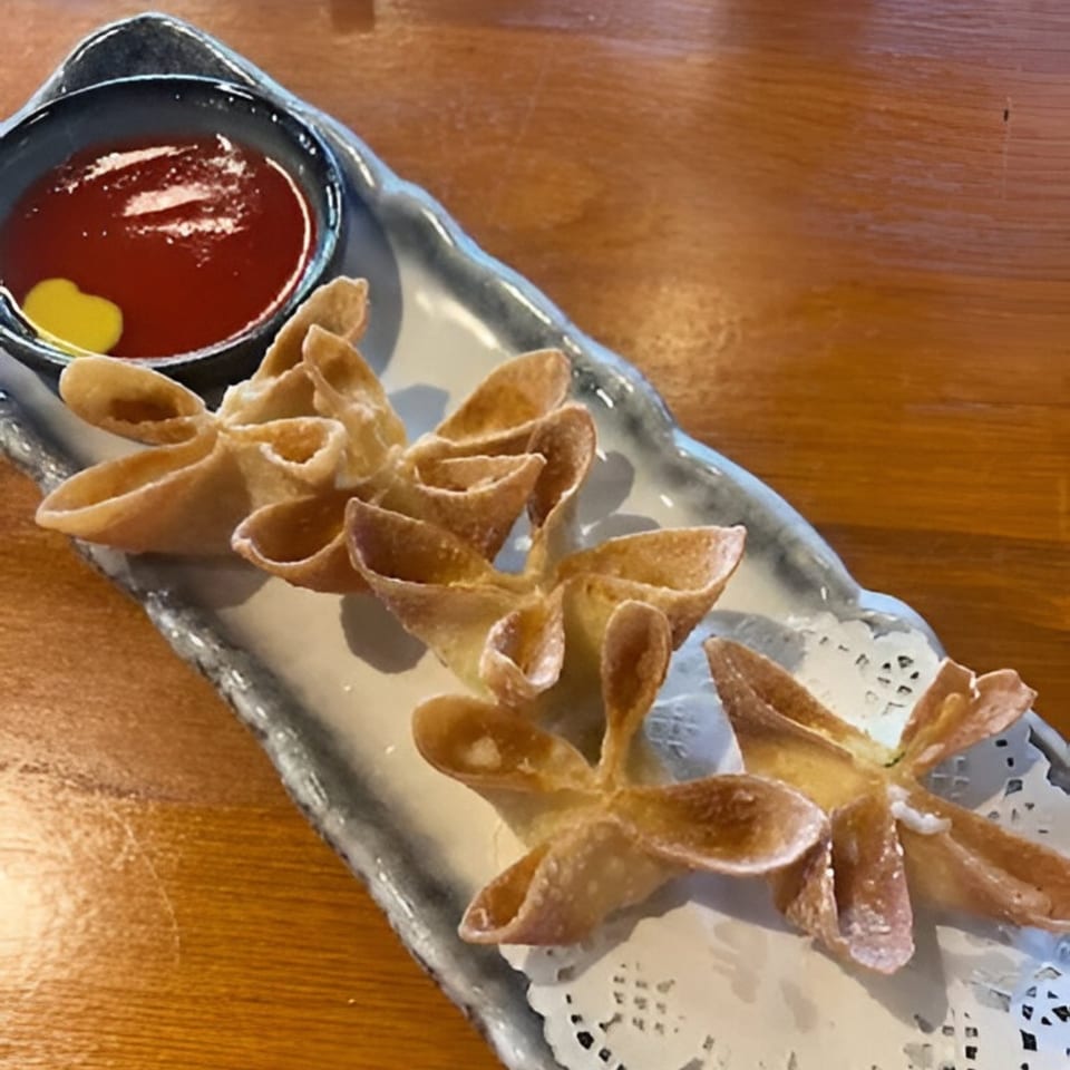 Crab rangoons with a side of red dipping sauce and yellow mustard on a gray plate.