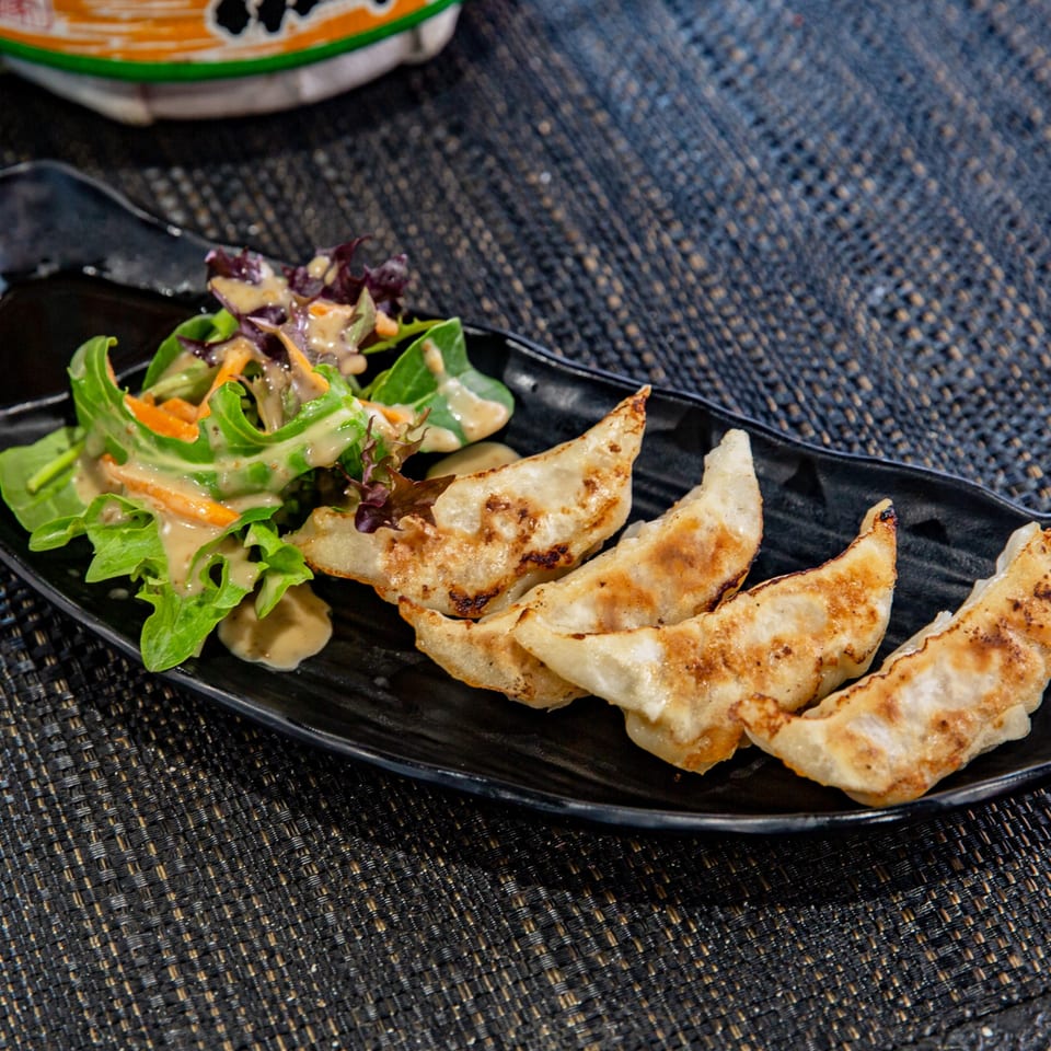 Golden-brown gyoza dumplings and a fresh green salad with dressing on a black plate.